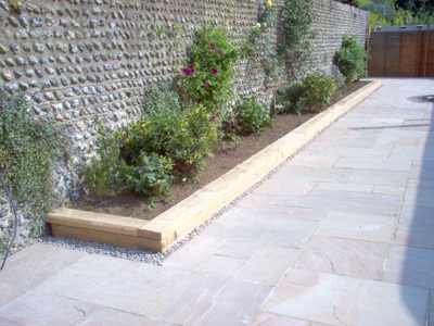 patio_rustington_indian_sandstone_flower_boarder_wooden_sleeper_surround_flint_wall.jpg